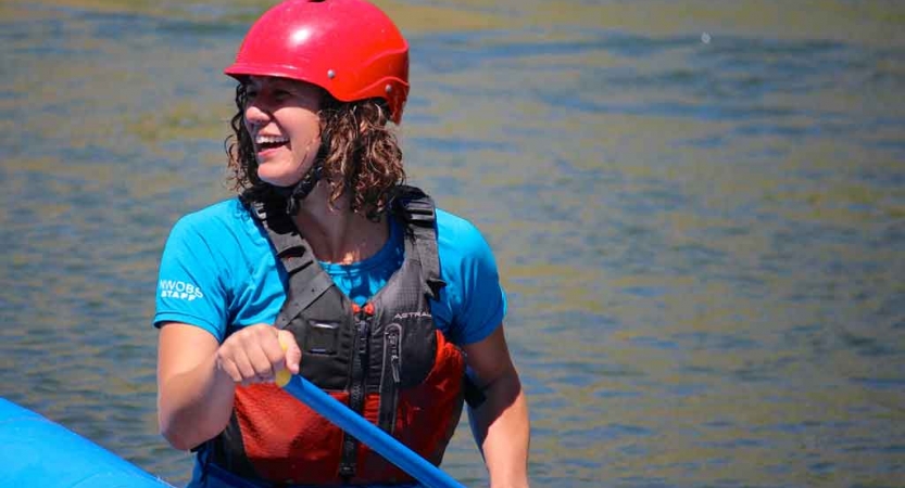 a person wearing rafting gear and holding a paddle smiles from a raft